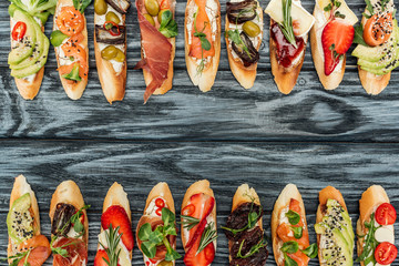 top view of italian bruschetta with prosciutto, herbs, salmon and vegetables on wooden table