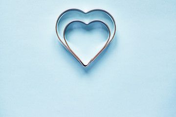 Two metal cookie cutters in heart shape on light blue background with copy space