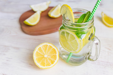 Mason jar glass of homemade lemonade with lemons, mint and green paper straw on wooden rustic background. Summer refreshing beverage.