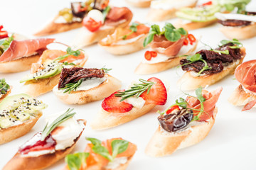 selective focus of italian bruschetta with dried tomatoes, prosciutto, avocado, strawberries and herbs