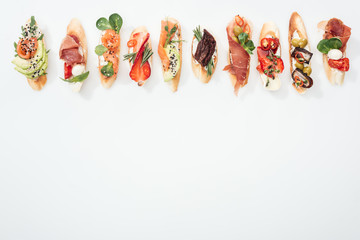 top view of traditional italian bruschetta with prosciutto, salmon, fruits, vegetables and herbs on white with copy space