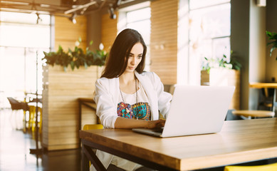 Beautiful girl working out a plan of the project and concept. Girl paints a website design on a laptop. student prints a message on the phone in the messenger. Development. Digital marketing