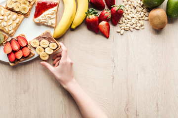 top view of woman holding fruit toast at wooden table with fresh ingredients