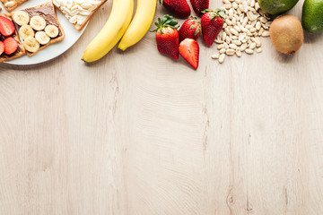 top view of bananas, strawberries, peanuts and toasts on wooden table with copy space