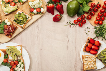 top view of toasts with vegetables, fruits and prosciutto with greenery and ingredients on wooden table