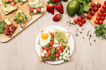 top view of ingredients and toasts with vegetables, fried egg and prosciutto on wooden table
