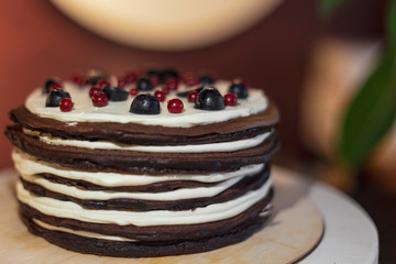 Cake from many thin brown pancakes in the form of pancakes stuffed with white cream and stopped with berries and fruits
