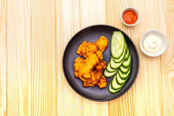 Chicken fried (nuggets) homemade on black plate with two sauces - mayonnaise and hot spicy sauce. On wooden background, top view