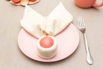 Easter bunny (rabbit) egg concept, table arrangement decoration. Pink (rosy) eggs with plate, fork, cloth vintage linen napkin on a stone background