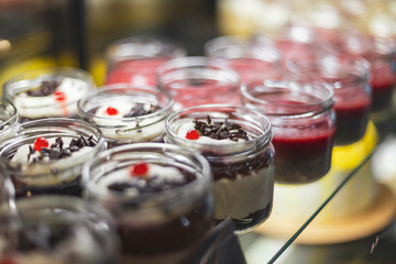Multicolored desserts in jars are located in a confectioner's refrigerator in a show-window
