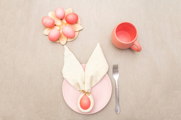 Easter bunny (rabbit) egg concept, table arrangement decoration. Pink (rosy) eggs with plate, fork,...