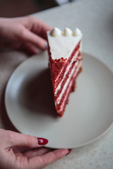 An appetizing slice of cake made from red cake biscuits with a white cream on a gray plate.