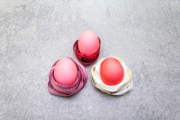 Easter concept pink (rosy) eggs in polka dot satin ribbon nests. On stone background in sunny rays