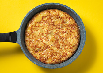 tortilla de patatas on skillet on yellow background, typical spanish dish.