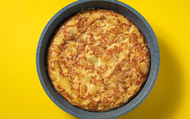 tortilla de patatas on skillet on yellow background, typical spanish dish.