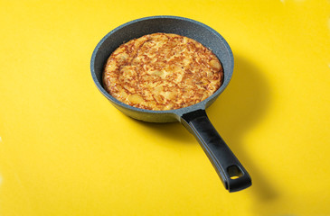 tortilla de patatas on skillet on yellow background, typical spanish dish.