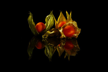 Several Physalis fruits (cape gooseberry) on a black background. The Physalis and its green leaves...