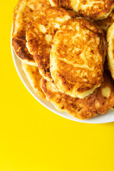 Pile of freshly fried homemade fluffy pancakes from cottage cheese on plate on bright yellow background. Appetizing golden crust. Trendy food poster recipe template. Home cooking baking