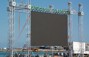 Big open-air black outdoor LED screen for public music event at sea shore, copyspace