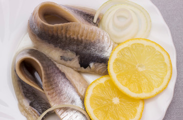 marinated herring fillet with onion and lemon on white plate, top view with copy space