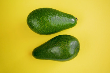  two ripe green beautiful avocados on a yellow background lie with a javelin