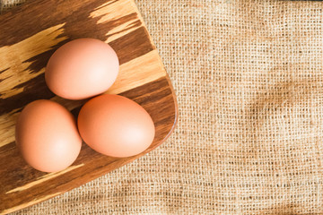 three brown eggs lie on a wooden plate on sackcloth