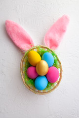 colorful eggs in a wicker basket, on a white background. Hare ears. Happy easter. Top view