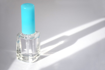 Closed bottle of clear nail polish for manicure. Clear transparent nail polish bottle with blue cap. Manicure concept. Sunbeam illuminates a bottle of nail polish with copy space, moke up.