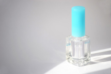 Bottle of clear nail polish on a light background. Clear transparent nail polish bottle with blue cap. Sunbeam illuminates a bottle of nail polish with copy space, moke up. Manicure concept.