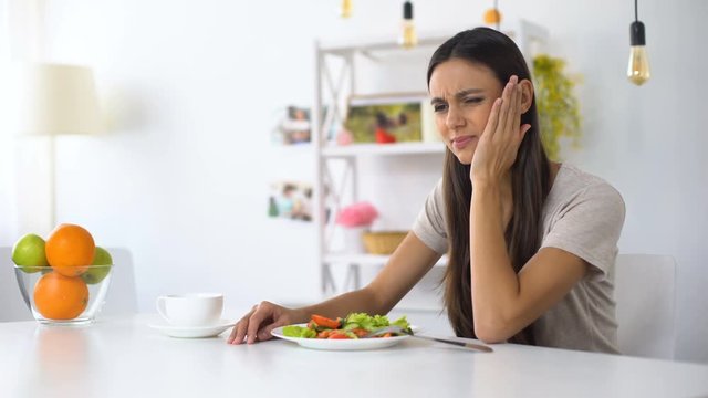Woman eating salad, feeling tooth ache from excess acid in products, health