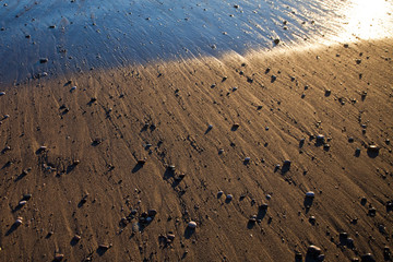 Sand and stones on the seashore after a surging wave in the sunset rays of the sun. background image. Tourism in Abkhazia.