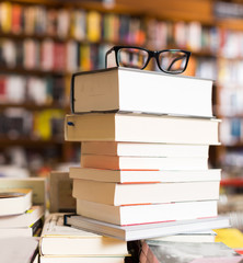 glasses on top of stack of books lying on table in bookstore