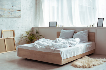 interior of bedroom with cozy bed, pillows, blanket, pictures and plant