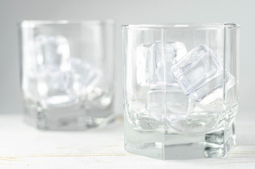 Empty glasses with ice cubes, white background, wooden backdrop