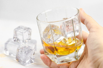 Glasses of scotch whiskey with ice cubes, white background, wooden backdrop