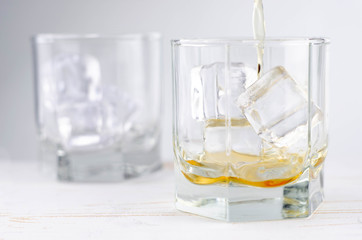 Two glasses of scotch whiskey with ice cubes, white background, wooden backdrop