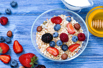 healthy muesli with raspberry, blueberry, strawberry, BlackBerry, hazelnut, milk and honey on blue wooden rustic table. Top view. homemade muesli or granola with honey, milk, fresh berries and nuts