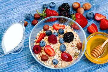 healthy muesli with raspberry, blueberry, strawberry, BlackBerry, hazelnut, milk and honey on blue wooden rustic table. homemade muesli or granola, fresh berries. Top view. Healthy diet.