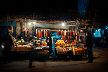 Night scene on the streets of Tbilisi, Georgia. Street sellers around corner selling traditional Georgian products with customers passing by. - Night image