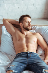 good-looking and muscular man lying on bed and looking away in bedroom