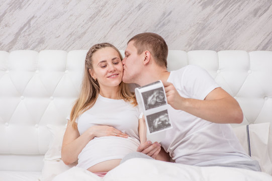 Pregnant woman and her young husband looking at ultrasound scan photo of unborn child