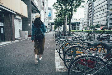 Parking for bicycles on the street rent a bike and walking around city in osaka japan. back view full length young asian woman in hat sightseeing busy urban residential area. female relax sunny day