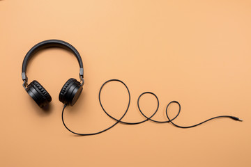 Photo of stylish modern black headphones over beige background.