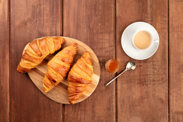 A photo of croissants, shot from the top on a dark rustic wooden background with coffee, jam, and copy space