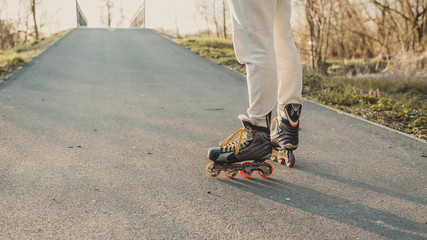  Quick movement of inline boots on the road at sunset. Outdoor inline skating on a trail beside the...