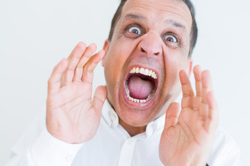 Middle age man shouting crazy with hands over mouth over white wall background