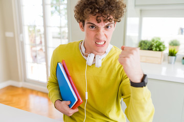 Young student man wearing headphones and holding notebooks annoyed and frustrated shouting with anger, crazy and yelling with raised hand, anger concept