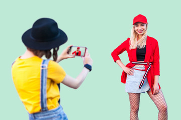 Capture the moment. Two stylish hipster girls in fashionable clothes having fun together, brunette woman making pictures of her best friend, positive friendship mood, photographer on work, Indoor