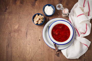 Bowl of red beetroot soup borscht with sour cream and bread crackers on rustic background