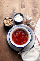 Bowl of red beetroot soup borscht with sour cream and bread crackers on rustic background